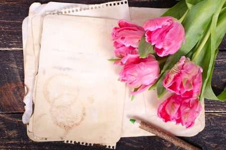 Pink tulips and vintage paper, pencil on a wooden background. Free space for your text.の写真素材