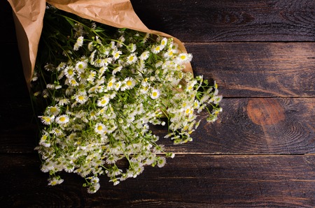 Bunch of Chamomiles flowers in craft paper on wooden background. Free space for your text.の写真素材