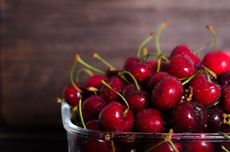 Fresh cherry fruits in a glass on a wooden table. Free space for your text.の写真素材