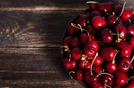 Cherries in a brown bowl on a wooden table. Free space for your text.の写真素材