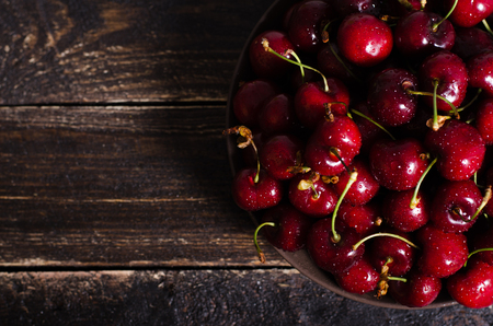Cherries in a brown bowl on a wooden table. Free space for your text.の写真素材