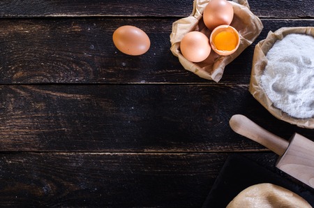 Ingredients for baking - dough, flour, wooden spoon, rolling pin, eggs, egg yolks on white background. Free space for your textの写真素材