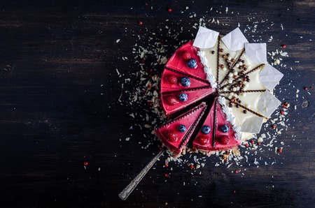 Delicious raspberry cake with fresh raspberries, blueberry, almond slices, rose pepper and chocolate cheesecake on black background.の写真素材