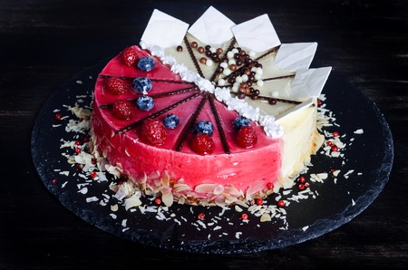 Delicious raspberry cake with fresh raspberries, blueberry, almond slices, rose pepper and chocolate cheesecake on black background.の写真素材