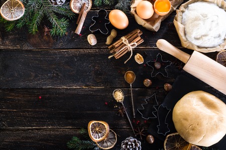 New year baking background - cones, fir tree, dough, flour, rolling pin, eggs, egg yolksover, spices, dry oranges, old dark wood background.の写真素材