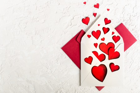 Valentine day. Red hearts and envelopes on white concrete background. Free space for your text.