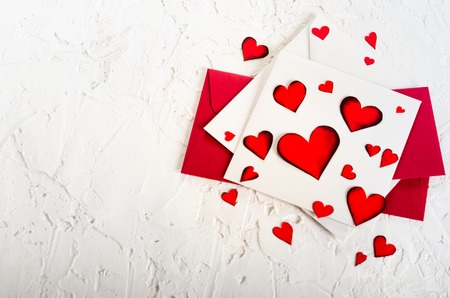 Valentine day. Red hearts and envelopes on white concrete background. Free space for your text.
