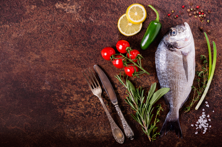 Fresh raw fish with lemon, herbs, onion, paprika, cherry tomatoes, onion, salt on rustic background. Healthy food concept. Free space for your textの写真素材