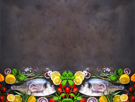 Fresh uncooked fish, dorado, sea bream with lemon, herbs, vegetables and spices on stone background. Top view. Banner.の写真素材