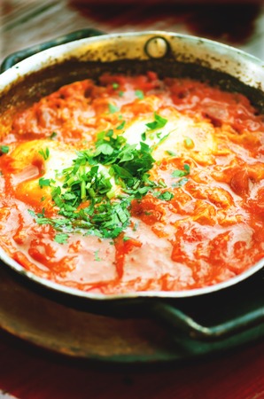 Shakshuka. Traditional jewish food and middle eastern cuisine recipe. Fried eggs, tomatoes, bell pepper and parsley in a pan. Close up, selective focus. Tonnen effectの写真素材