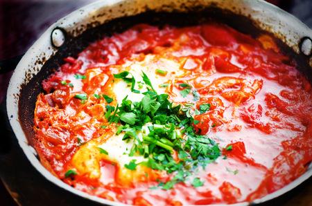 Shakshuka. Traditional jewish food and middle eastern cuisine recipe. Fried eggs, tomatoes, bell pepper and parsley in a pan. Close up, selective focus. Homemade breakfast.の写真素材