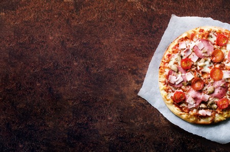 Fresh italian pizza with mushrooms, ham, tomatoes, cheese on on backing paper, dark background. Copy space. Homemade with love. Fast delivery. Recipe and menu. Bannerの写真素材