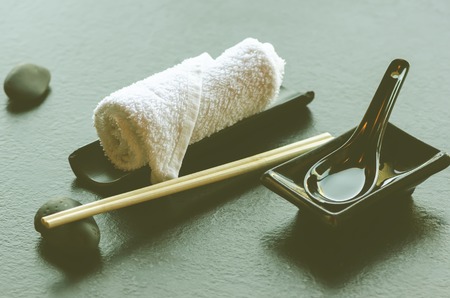 Japanese, asian food utensils - pair of chopsticks, hot weat towel, ceramic black spoon, dark stone in restaurant, cafe.の写真素材