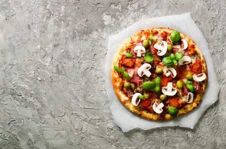 Fresh italian pizza with mushrooms, ham, tomatoes, cheese on on backing paper, grey concrete background. Copy space. Homemade with love. Fast delivery. Recipe and menu. Top view.の写真素材