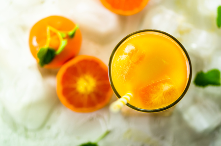 Fresh orange juice in glass and tangerines with mint, ice on white background. Top view, copy space. Hot summer day. Holidayの写真素材