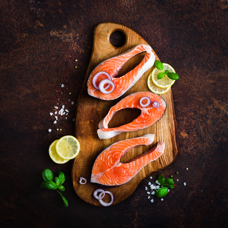 Raw fresh salmon fillet with aromatic herbs, spices, salt and lemon on wooden background. Healthy food concept, diet or cooking, protein product. Copyspace.の写真素材