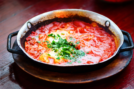 Shakshuka. Traditional jewish food and middle eastern cuisine recipe. Fried eggs, tomatoes, bell pepper and parsley in a pan. Close up, selective focus. Tonnen effectの写真素材
