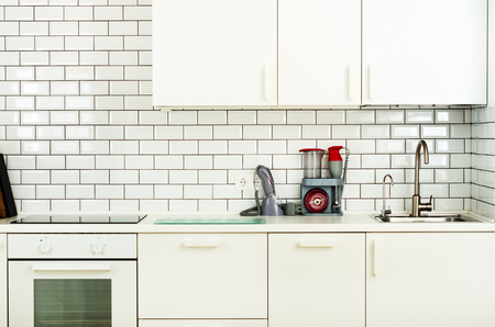 White minimalistic kitchen interior and design. Tile wall background. Household appliances - blender, vacuum machine, modern stove, dishwasher, oven, table, faucet mixer.の写真素材