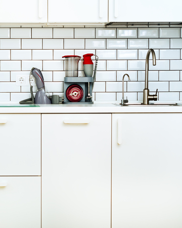 White minimalistic kitchen interior and design. Tile wall background. Household appliances - blender, vacuum machine, modern stove, dishwasher, oven, table, faucet mixer.の写真素材