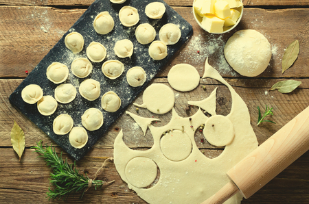 Ingredients for making pelmeni, ravioli, dumplings - dough, rosemary, rolling pin, canvas thread, butter, bay leaf. Top view. Wooden background.の写真素材