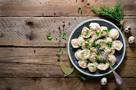 Boiled prepared homemade russian pelmeni, dumplings, ravioli with meat on grey plate with fresh parsley, pepper, wooden rustic background. Top view. Copyspace.の写真素材