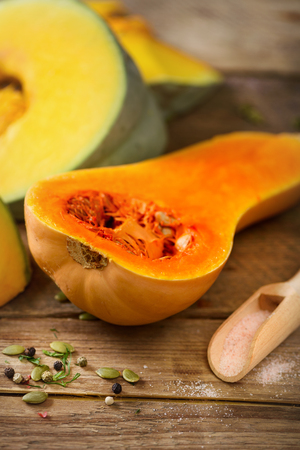 Cut ripe orange pumpkin with seeds and herbs on rustic wooden background. Vegetarian and raw organic healthy food concept, diet. Top view, copy spaceの写真素材