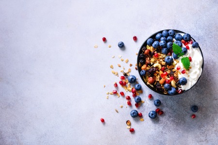 Tasty homemade granola, yogurt, fresh organic berries, pomegranate, mint on grey concrete background with copy space, top view.の写真素材