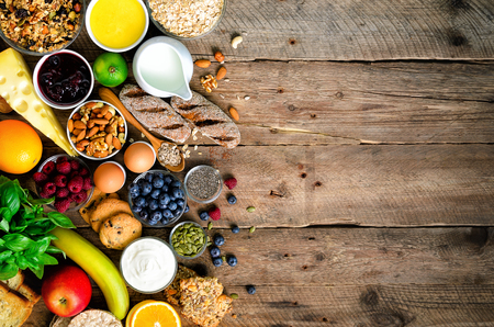Healthy breakfast ingredients, food frame. Granola, egg, nuts, fruits, berries, toast, milk, yogurt, orange juice, cheese, banana, apple on wooden rustic background, top view, copy spaceの写真素材