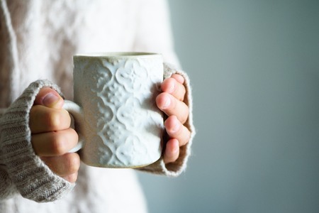 Famale hands holding a cozy ceramic handmade mug with coffe. Winter and Christmas home time concept. Lifestyle. Copy spaceの写真素材