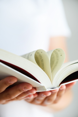 Book with opened pages and shape of heart in girl hands. Copy space. Love conceptの写真素材