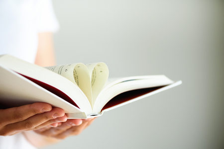 Book with opened pages and shape of heart in girl hands. Copy space. Love conceptの写真素材