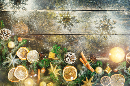 Christmas greeting card with gifts, candle, cones, cinnamon sticks, dry orange, green tree over old dark wood background. Top view with copy space for you text. Snow and bokehの写真素材