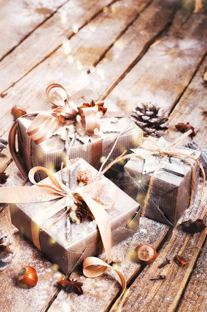 Gift boxes on old wooden background with silver stars, cones, hazelnut, anise, tape, ribbon, snowflakes. Top view, copy space, light bokeh, snow effect, toned.の写真素材