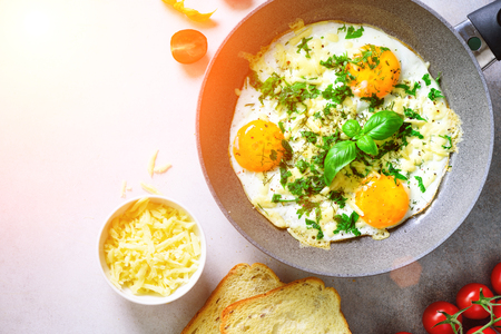 Sunny morning. Breakfast with fried eggs in pan, herbs, spices, cherry tomatoes, cheese toasts, basil on grey concrete stone background. Copy space, top view, flat lay, sunlightsの写真素材