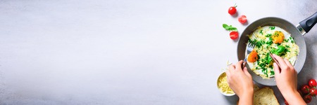 Girl hands above frying pan with three cooked eggs, herbs, cheese, tomatoes. Woman is making breakfast. top view. Copy space. Banner, top view, flat layの写真素材