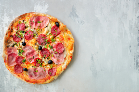 Fresh italian pizza with mushrooms, ham, tomatoes, cheese, olive, pepper on grey concrete background. Copy space. Top view.の写真素材