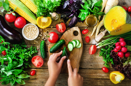 Woman hands cutting vegetables on wooden background. Vegetables cooking ingredients, top view, copy space, flat layの写真素材