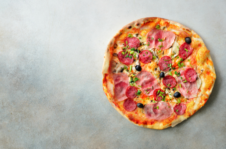 Fresh italian pizza with mushrooms, ham, tomatoes, cheese, olive, pepper on grey concrete background. Copy space. Top view.の写真素材