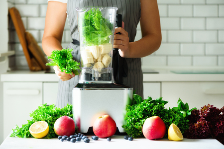 Woman blending lettuce leaves, spinach, aplles, berries, bananas. Homemade healthy green smoothie. White kitchen designの写真素材