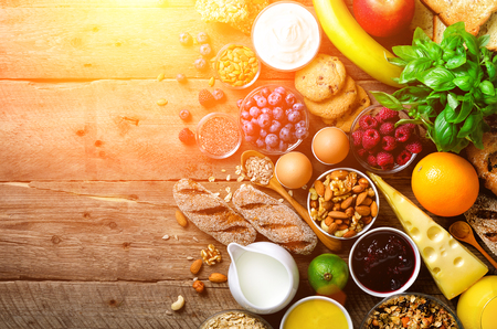 Healthy breakfast ingredients, food frame. Granola, egg, nuts, fruits, berries, toast, milk, yogurt, orange juice, cheese, banana, apple on wooden rustic background, top view, copy spaceの写真素材