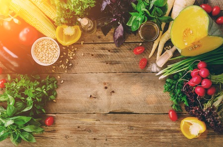 Vegetables on wooden background. Herbs, basil, onion, pumpkin, pine nuts, tomatoes, corn, radish, eggplant, bell pepper, salt, spices, oil, spinach, parsley, lettuce leaves. Top view, copy spaceの写真素材