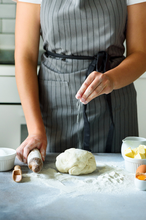 Female hands kneading dough, baking background. Cooking ingredients - eggs, flour, sugar, butter, milk, rolling pin on white style kitchen. Copy spaceの写真素材