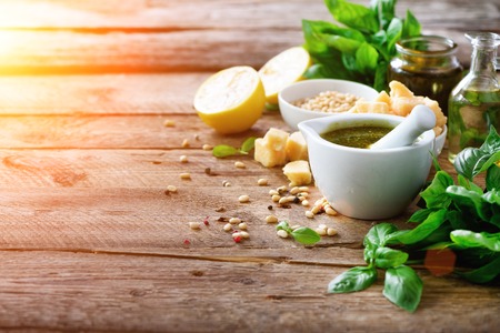 Ingredients for homemade pesto - basil, lemon, parmesan, pine nuts, garlic, olive oil and salt on rustic wooden background. Top view, flat lay, copyspace, sunlightsの写真素材