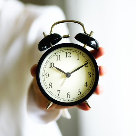 Classic black alarm clock in a hand. Sunny morning light. Copy spaceの写真素材