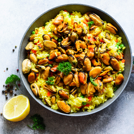 Traditional spanish seafood paella in pan rice, peas, shrimps, mussels, squid on light grey concrete background. Top view, copyspace.の写真素材