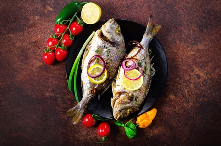 Cooked baked grilled fish, dorado, sea bream with lemon, herbs, vegetables and spices on rustic...