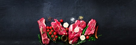 Raw fresh meat steak with cherry tomatoes, hot pepper, garlic, oil and herbs on dark stone, concrete...