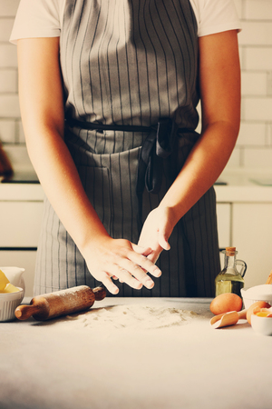 Female hands kneading dough, baking background. Cooking ingredients - eggs, flour, sugar, butter, milk, rolling pin on white style kitchen. Copy spaceの写真素材