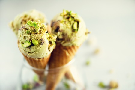 Green ice cream in waffle cone with chocolate and pistachio nuts on grey stone background.の写真素材