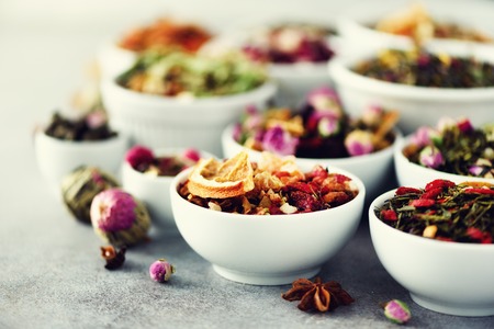 Assortment of dry tea in white bowls. Tea types backgound: green, black, floral, herbal, mint, melissa, ginger, apple, rose, lime tree, fruits, orange, hibiscus, raspberry, cornflower, cranberry.の写真素材